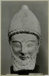 Limestone head of a bearded male figure wearing a tall patterned cap, shown on a dark stand.