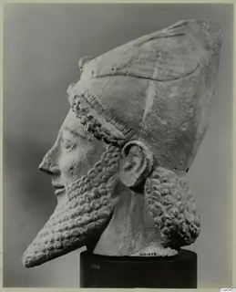 Limestone head with a curled beard in profile, facing left, wearing a tall headdress