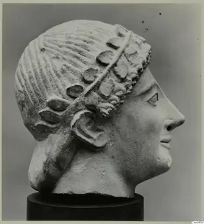 Limestone head sculpture in profile, with carved hair and a wreath or band of leaves over the forehead and ear.
