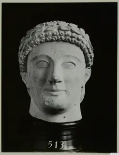 Limestone head with a band of curled hair, photographed against a black background on a dark stand.