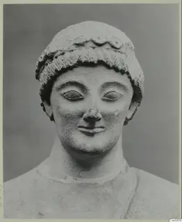 Limestone head of a statue with rows of curls and a band across the forehead, shown from the front.