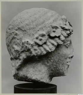 Limestone head sculpture in side view, face turned to the right, on a dark cylindrical stand.