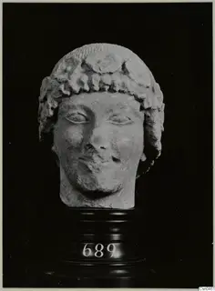 Limestone head, Cypro-Greek I, with curled hair, shown on a dark stepped stand with a number label