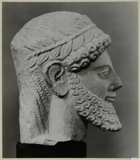 Limestone head with a curled beard and leafy band in the hair, shown in profile on a dark base