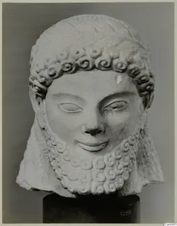 Limestone head of a bearded statue with curled hair and beard, on a dark stand