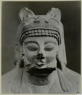 Limestone sculpture of a bust wearing a headdress with upright projections; the nose and mouth are broken away.