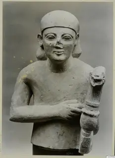Bust-length limestone sculpture of a figure in a close-fitting cap, one arm across the chest, gripping a fluted upright object