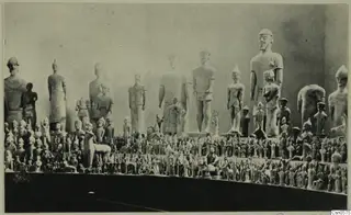 Many pale stone statues and small figurines arranged in tiers on shelves in the Cyprus Museum display.