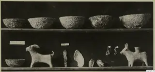 Five rough-surfaced bowls on an upper shelf, with a goat figurine, a bull-like figurine and small finds on a lower shelf