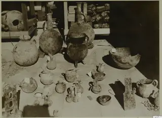 Pottery jars, jugs and bowls set out together on a floor, with paper tags tied to several of the pieces