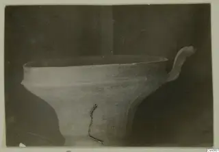 Bowl with a wide open mouth and an upturned handle on its right side, photographed against a dark background