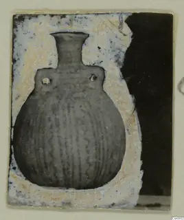 Globular pot with a tall narrow neck, two small lugs on the shoulder and vertical grooves on the body, shown in a window-cut card mount