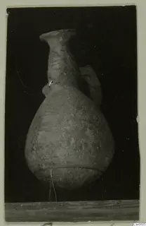Pottery vessel with a flared rim, single handle and painted pattern, photographed against a black background