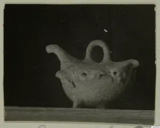 Pottery vessel with a loop handle, a raised spout and a patterned body, shown against a dark background.