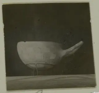 Bowl with a square pattern and a long projection on one side, standing on a wire support against a dark background