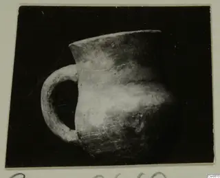 Pottery jug with a flared rim and a single loop handle, shown against a dark backdrop.