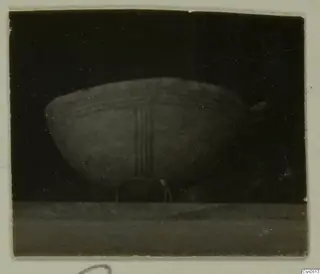 Pottery bowl with horizontal bands and three vertical stripes painted on its body, shown against a dark background.
