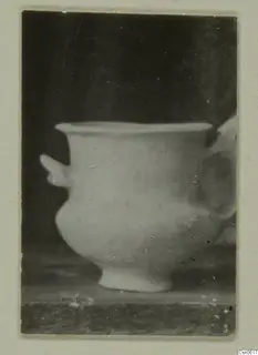 Small footed vessel with a side lug and a blurred handle, photographed on a dark background and mounted on a card