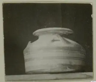 Rounded pottery vessel with horizontal grooves around the body and a broad flat rim, on a pale surface