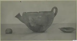 Pottery vessel with a spout and loop handle, shown with two small objects on a plain surface, find from Cyprus