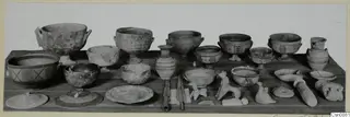 Jugs, bowls, lids and small figurines of pottery laid out on a wooden table