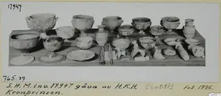 Clay bowls, jugs, lids and small figurines arranged on a wooden table.