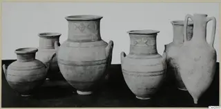 A row of painted pottery jars and a two-handled vessel with banded decoration, photographed on a dark surface