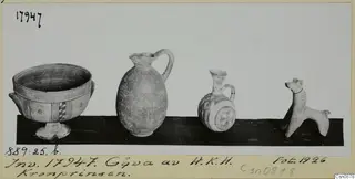 Footed bowl, two jugs and a small animal figurine standing on a dark shelf