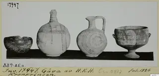 Four painted pottery vessels on a dark board: a bowl, a tall striped bottle, a jug with a loop handle and a footed bowl.