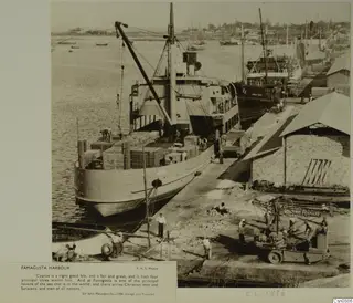 Famagusta harbour with a cargo ship being loaded by a crane, workers on the quay and a truck beside a warehouse