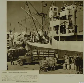 Wooden crates being loaded from a quay onto a lorry and a cart beside a cargo ship at Famagusta