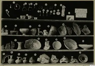 Finds from Tomb 2 at Lapithos Markides on four wooden shelves, each piece marked with a round numbered tag.