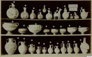 Pottery jugs, flasks and bowls from Lapithos Markides T.2, arranged in three rows on shelves