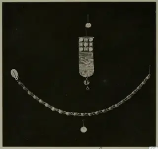 Necklace of curved segments and a rectangular pendant with inset elements, laid out on a black background.