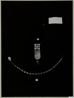 Necklace of beads and a rectangular inlaid plaque with a pendant, laid out on a black background