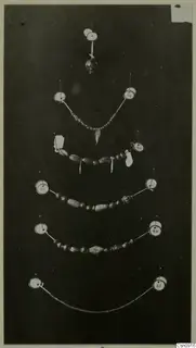 Several strings of beads and a small pendant pinned out on a dark background, each with a round number label.