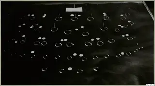 Many small rings, twisted wire coils and flat discs of jewellery spread across a dark surface.