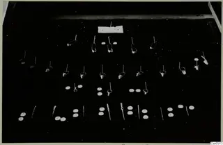 Small jewellery items laid out in rows on a dark cloth: hoop earrings, flat discs with holes and pins.