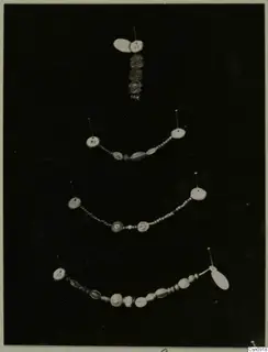 Four strands of beads and jewellery pinned on a dark background, each with a small paper tag.
