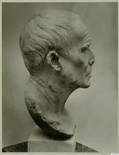 Stone sculpture of a man's head and neck in profile, facing right, on a pale pedestal