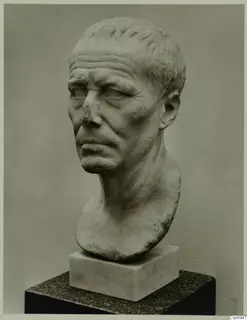 Carved bust of a man with curled hair and a broken nose, set on a pale block base and dark pedestal
