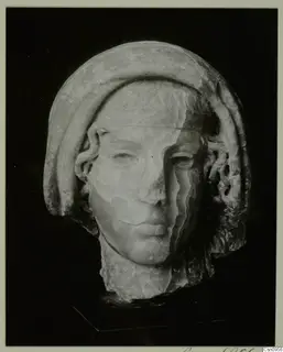 Carved stone head of a figure with a smooth, close-fitting band over the hair, photographed against a black background.