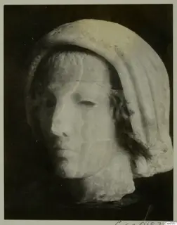 Stone head of a female figure with a draped veil, face turned to the left, against a dark background