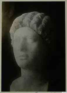 Marble head of a woman with wavy hair swept back, photographed against a dark background.