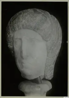 Carved stone head of a figure with layered hair, mounted on a round base, photographed against a black background.