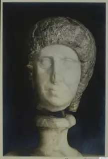 Marble head of a woman with a layered hairstyle, mounted on a carved base against a dark background.