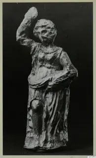 Standing figure with one arm raised, photographed against a dark background