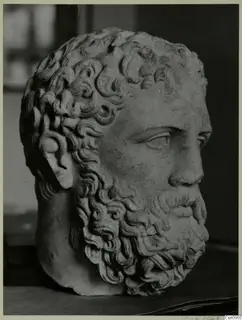 Carved stone head of a bearded man with deeply curled hair and beard, photographed against a dark background