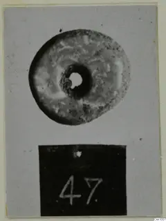Perforated stone disc with a central hole, photographed above a black number label.