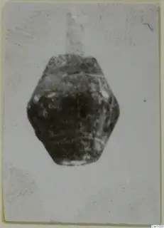 Dark stone bead from Amathus, squat and faceted, shown centred on a pale card
